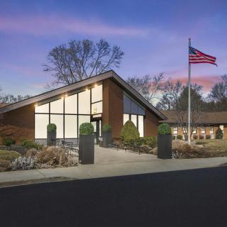 A modern building with large windows at sunset, accompanied by a flagpole displaying the American flag.