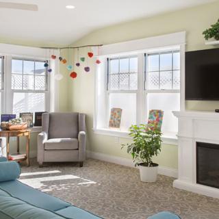 A cozy living room with modern furniture, bright sunlight streaming in through large windows, and a neatly arranged decor.