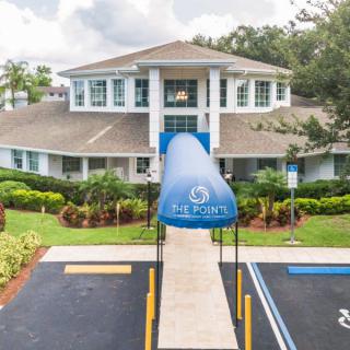 A well-maintained building with a blue awning at the entrance, surrounded by landscaped greenery.
