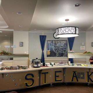 A buffet setup in a restaurant with various food items, prominently featuring steak.