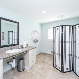 A modern, minimalist bathroom with a large vanity mirror and a partition.