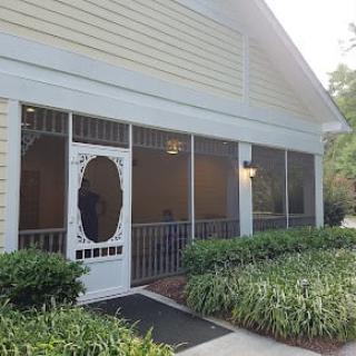 A quaint building with a screened porch and surrounding garden.