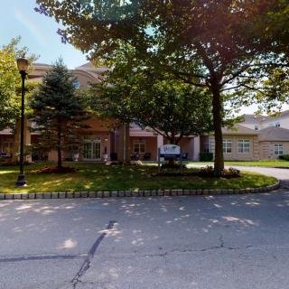 A view of a residential building surrounded by trees with a driveway and lamp post.