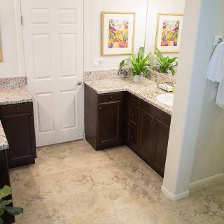 A modern bathroom featuring a double vanity, granite countertops, decorative plants, and framed artwork.