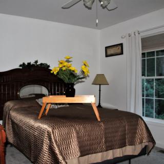 A cozy bedroom with a bed featuring a breakfast tray and flowers, accompanied by a lamp and window with curtains.