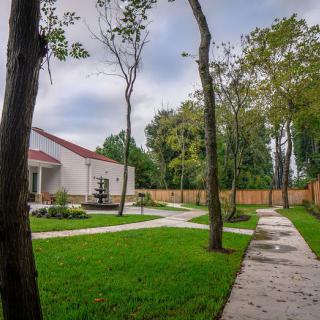 A serene backyard with a well-maintained garden, featuring a house, trees, and a concrete pathway surrounded by lush grass.