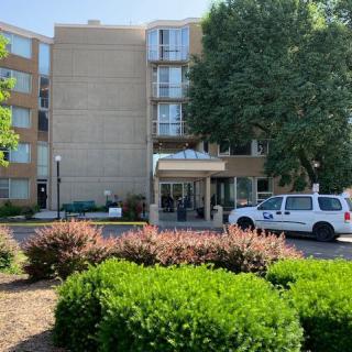 The entrance of a hotel with a car parked nearby and surrounding greenery.