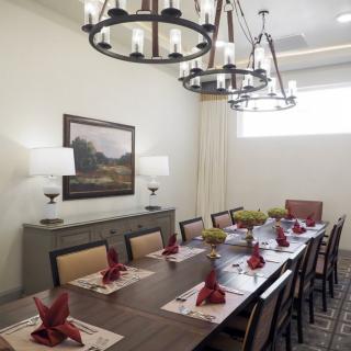 A well-decorated dining room featuring a long table with red napkins, chandeliers, and wall art.