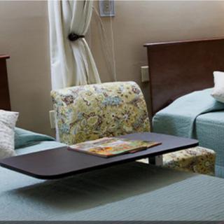 A hospital room with two medical beds, an overbed table, and a floral-patterned chair.
