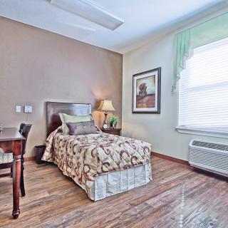 A cozy bedroom with a single bed, decorated with patterned bedding and a bedside lamp on a wooden floor.