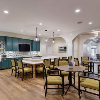 A modern open-space kitchen and dining area with teal cabinets, a large island counter, and elegant pendant lighting.