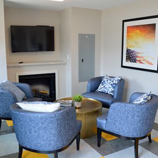 A modern living room featuring a cozy seating area with blue chairs, a coffee table, a fireplace, and contemporary artwork.