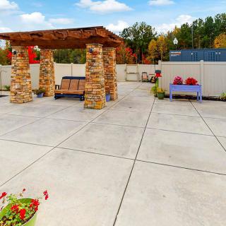 A spacious outdoor patio featuring a pavilion with stone pillars and benches, set against an autumn landscape.