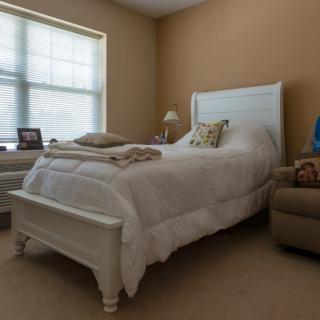 A cozy bedroom featuring a neatly made bed with pillows, a bedside lamp, and natural light coming through the window.