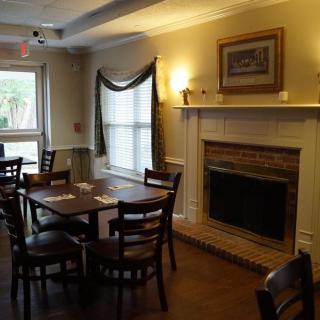 A cozy restaurant interior featuring wooden tables and chairs, a fireplace, and large windows.