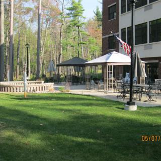 A serene outdoor setting featuring a gazebo, patio furniture, and a nearby building surrounded by lush greenery.