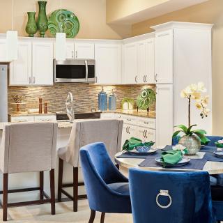 A modern kitchen and dining area featuring white cabinets, blue chairs, and a well-set table with decorative green accents.