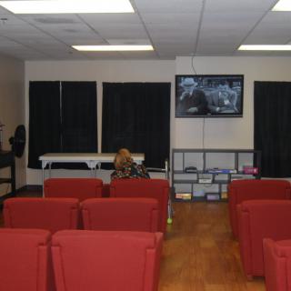 A spacious waiting room with red chairs, a television mounted on the wall, and black curtains covering the windows.