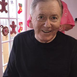 A smiling man indoors with holiday decorations in the background.