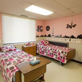 A cozy bedroom with two neatly made beds featuring pink and patterned bedspreads, decorated with wall art and a large window letting in natural light.