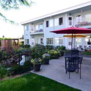 A tranquil outdoor patio area with seating, surrounded by a lush garden next to a residential building.