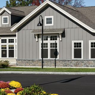 A modern residential building with gray siding, multiple windows, and a landscaped driveway.
