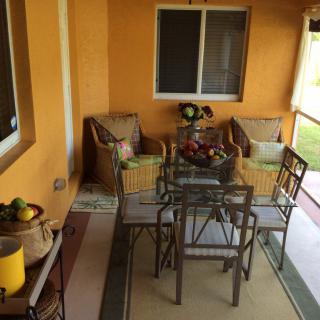 A cozy outdoor patio with a glass dining table and chairs, surrounded by comfortable seating and decorative plants.