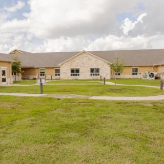 A single-story building with a grassy courtyard and cloudy sky.