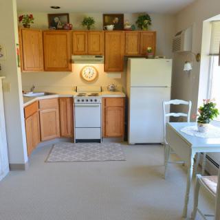 A cozy kitchen with wooden cabinets, a small stove, and a dining table by the window.