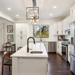 A modern kitchen with white cabinets and a central island, featuring stainless steel appliances and dark wood flooring.