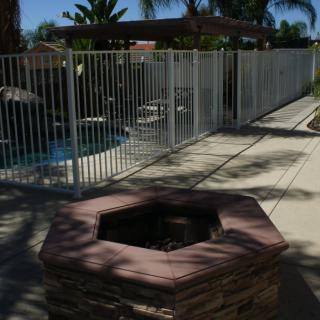 An outdoor patio area featuring a fire pit and fenced swimming pool under clear skies.
