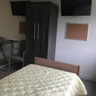 A simple and functional room featuring a bed, wardrobe, and workspace.