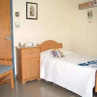 An empty hospital room with a single bed and wooden furniture.