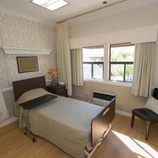 A clean and bright hospital room with a single bed, chair, and large windows.