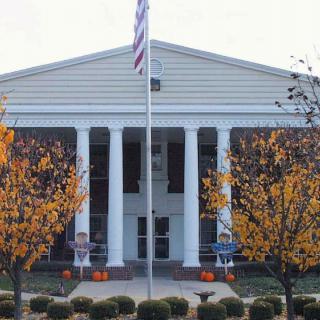 A symmetrical building with white columns, a flagpole in front, and trees with autumn foliage.