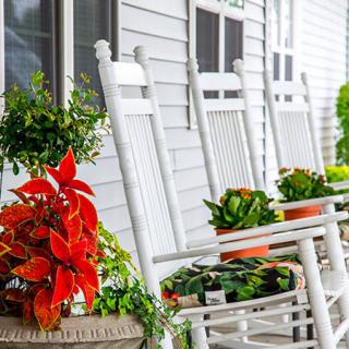 A cozy porch with white rocking chairs and colorful potted plants.