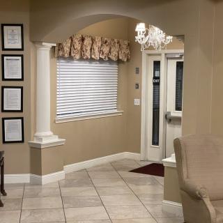 A cozy entryway featuring classic columns, elegant drapery above a window with blinds, and a chandelier providing warm lighting.