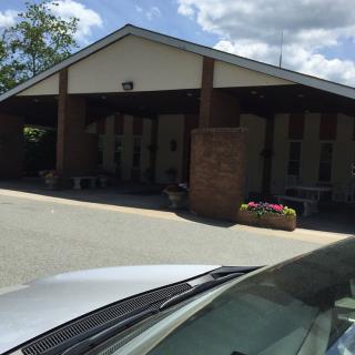 A building with a covered entryway and a parked car in the foreground on a sunny day.