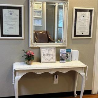 A stylish interior featuring a white console table with decorative items, a mirror, and framed certificates on the wall.