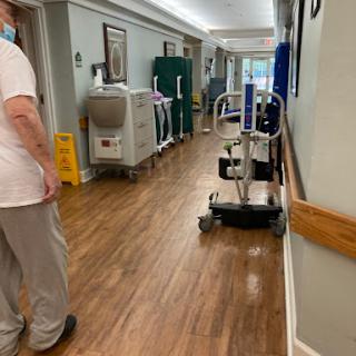 A staff member walks through a hospital hallway, passing by medical equipment and a cleaning sign.