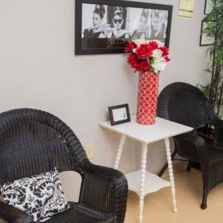 A cozy seating area with wicker chairs, a white table, and a red vase with flowers, complemented by wall art.