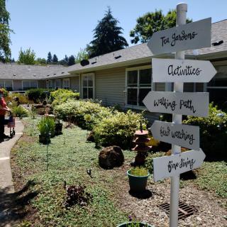 A garden scene with a signpost pointing to various activities and locations, surrounded by lush greenery.