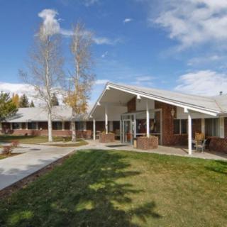 A modern residential building with a sloped roof, surrounded by trees and a well-maintained lawn under a partly cloudy sky.