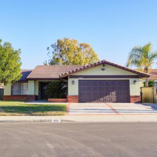A suburban one-story house with a driveway and garage, surrounded by trees and a well-maintained lawn.