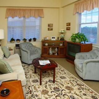 A cozy living room with traditional furnishings, featuring comfortable sofas and armchairs, a patterned carpet, and decorative curtains.