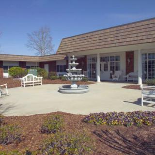 A sunny courtyard with a central fountain, surrounded by benches and landscaping in front of a building.