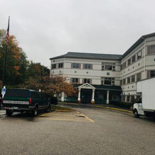 A commercial building with vehicles parked in front under a cloudy sky.