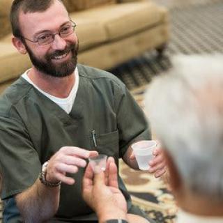 A caregiver assisting an elderly person, offering a glass of water with a smile.