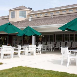An outdoor patio area with white tables and chairs under green umbrellas.