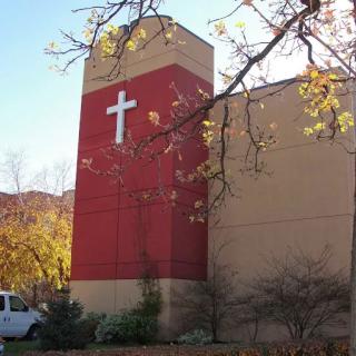 A church building with a prominent cross on its facade surrounded by autumn trees.